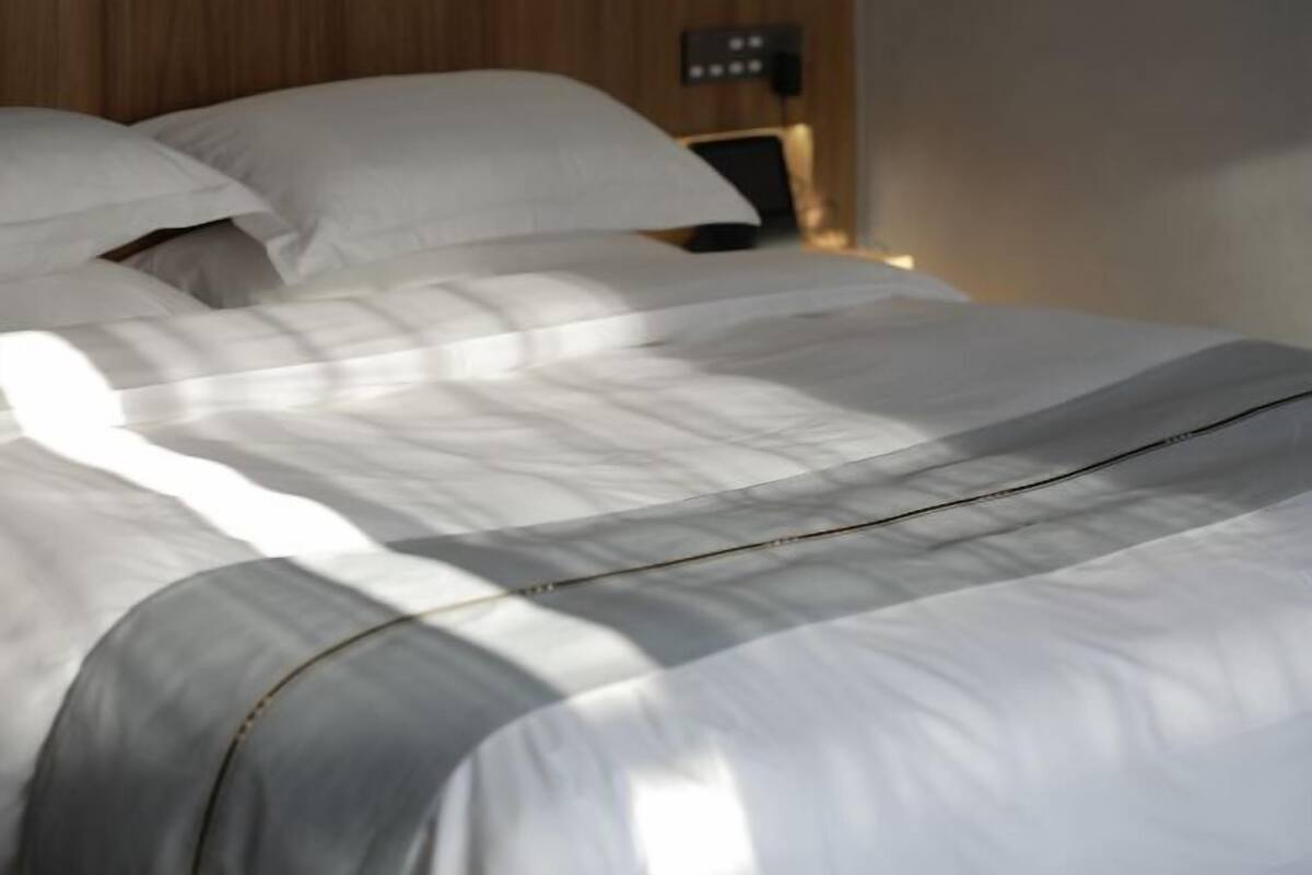 Un lit bien fait, avec du linge de lit blanc et une couture visible.