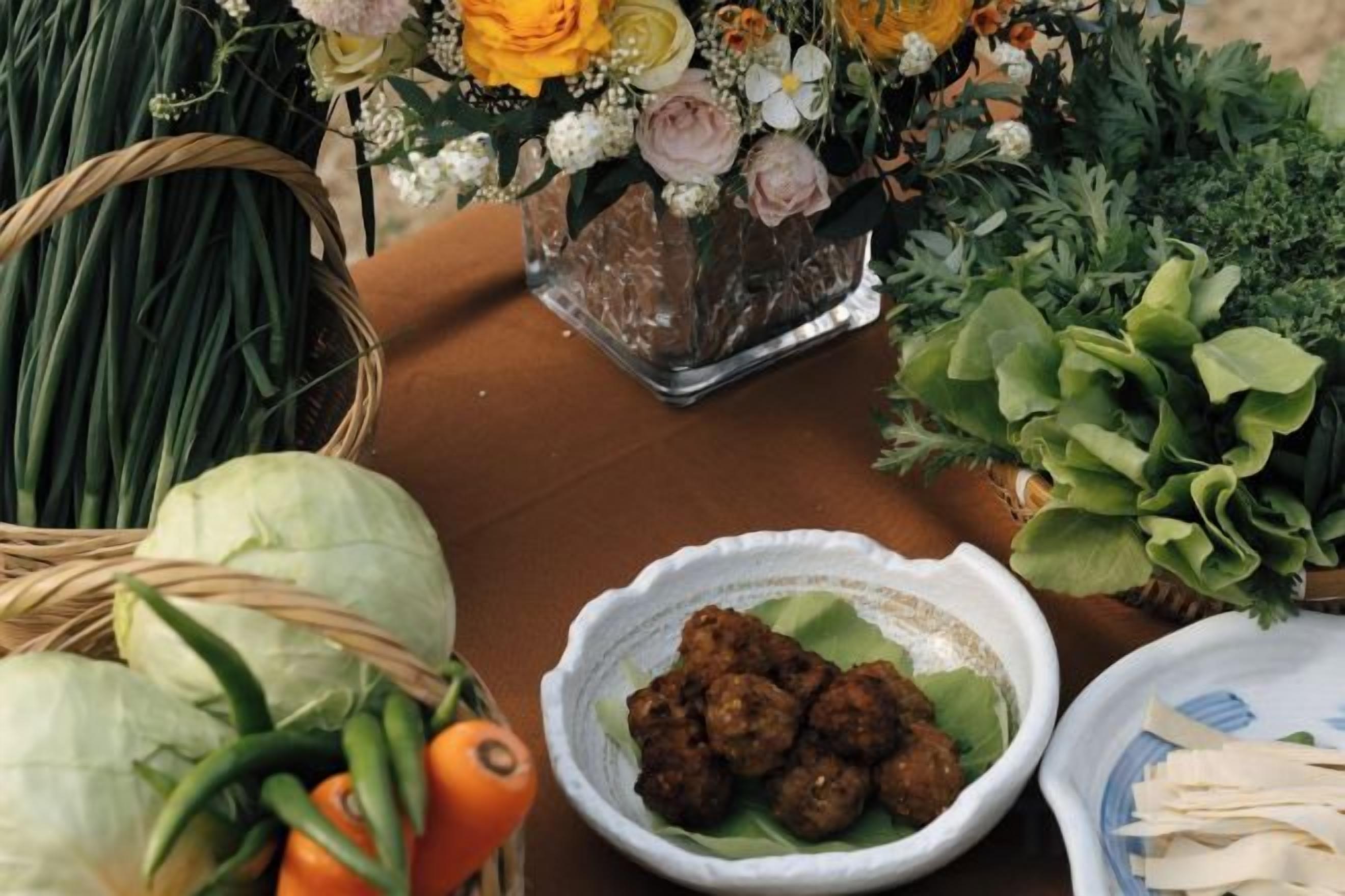 Una mesa con comida, un tazón de albóndigas y un florero con flores.