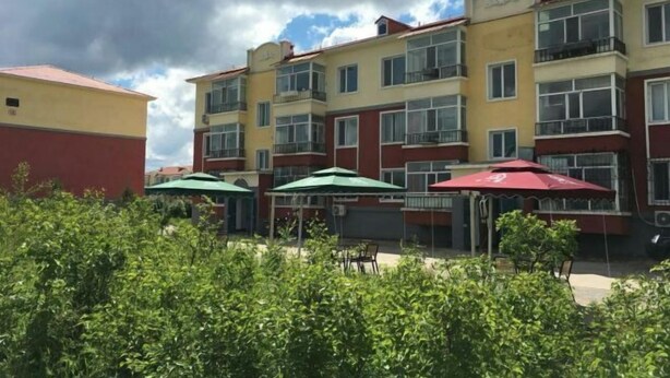 A multi-story hotel with balconies, outdoor seating with umbrellas, and a garden area in the foreground. - Tahe Eighteen Post Residence (Tahe)