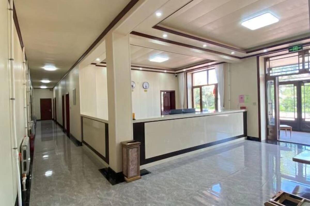 A hotel lobby with a reception desk, a long corridor, and a glass door leading outside.