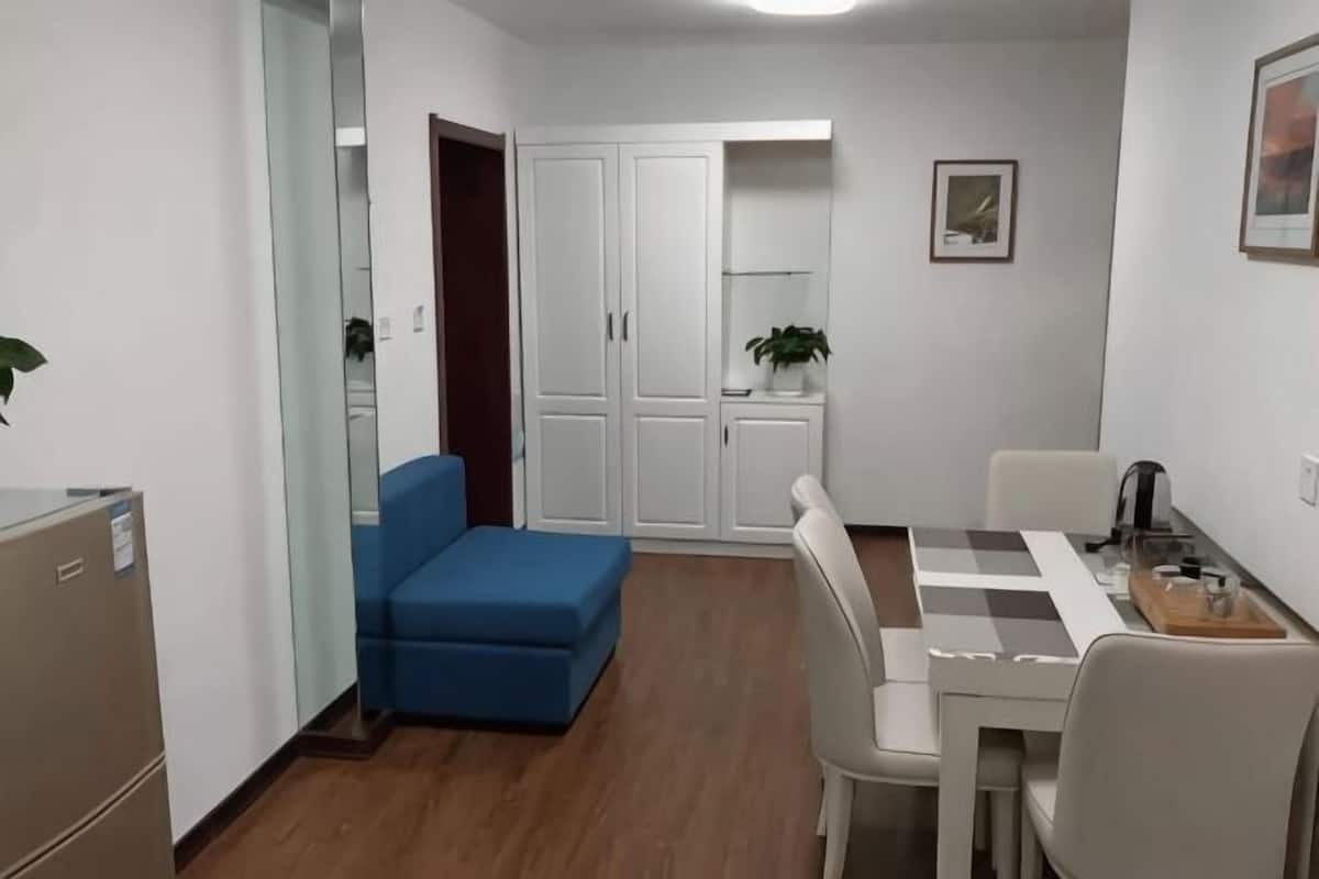 A compact room with a desk, chair, and a small blue sofa. There is a wardrobe with a mirror and a potted plant.