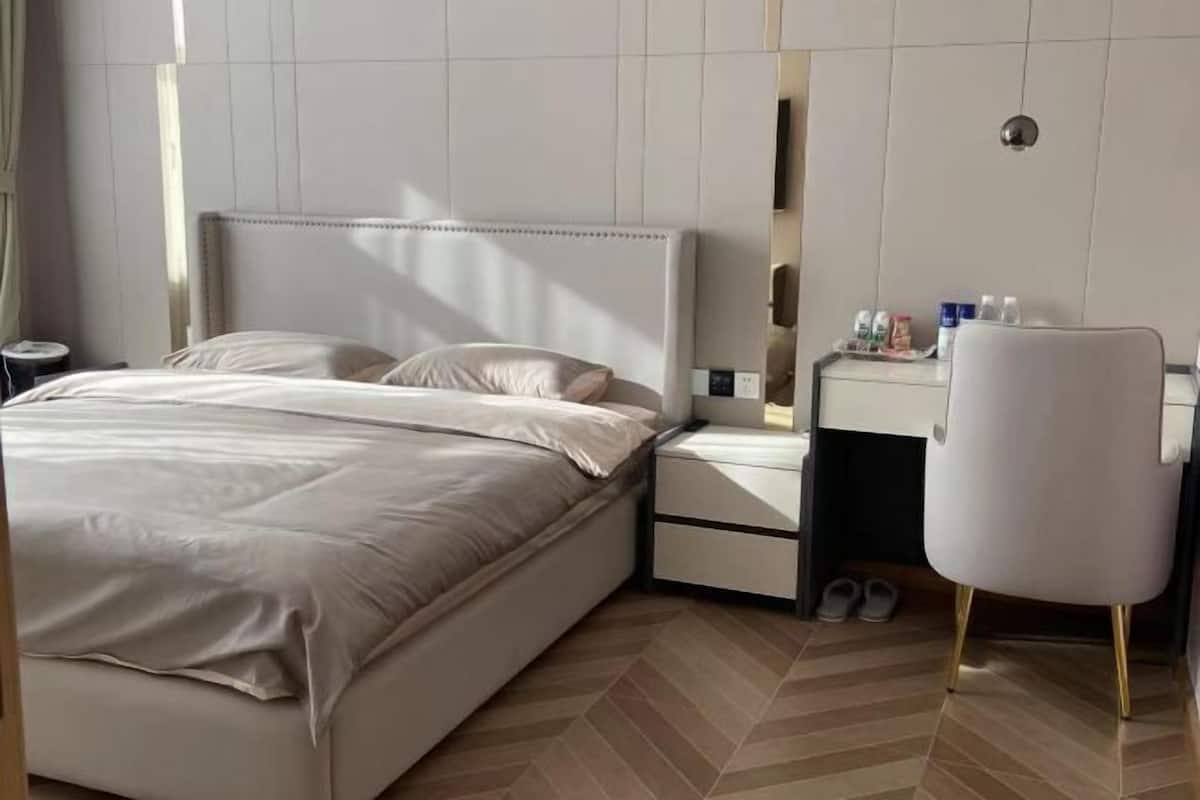 A hotel room with a bed, bedside table, chair, and a small desk with toiletries.