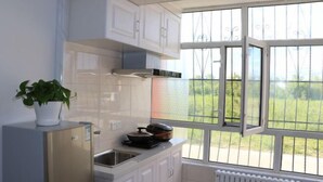 A modern kitchen with white cabinets, a built-in oven, and a window with a view of greenery. - Tahe Eighteen Post Residence (Tahe)