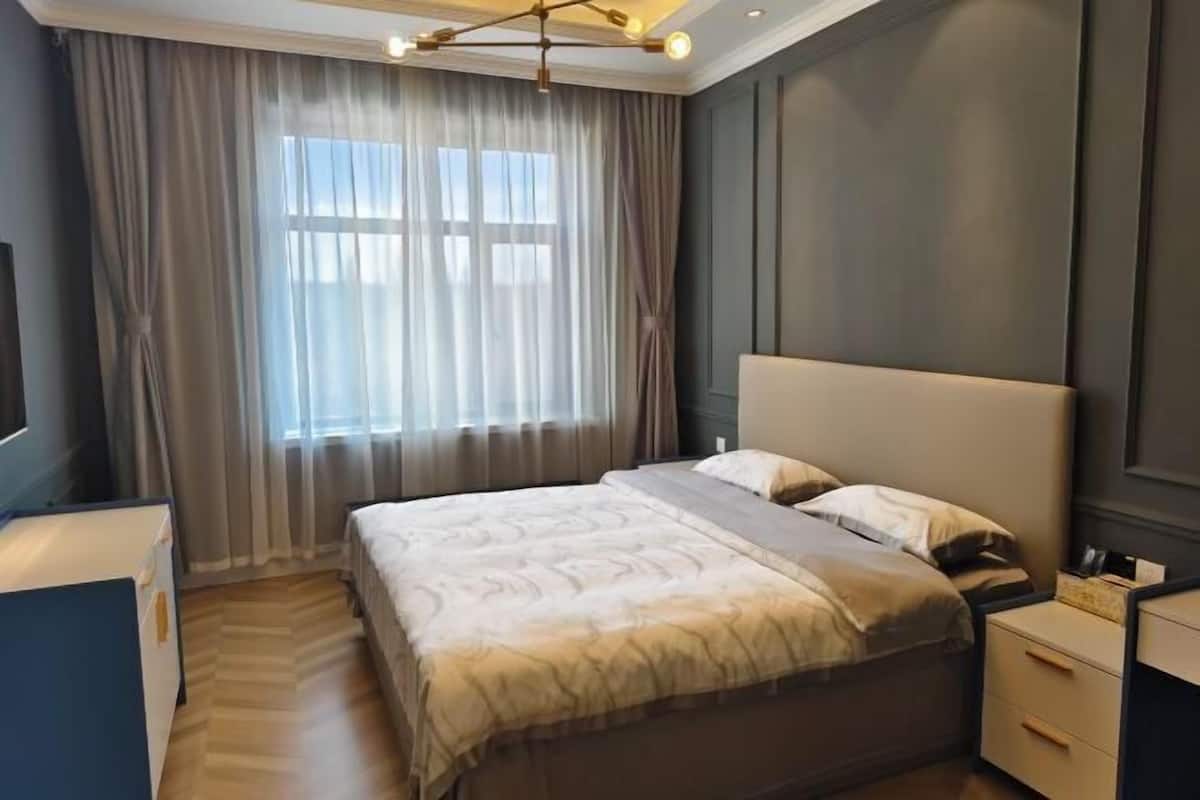 A modern hotel room with a large bed, a desk, and a window with curtains.