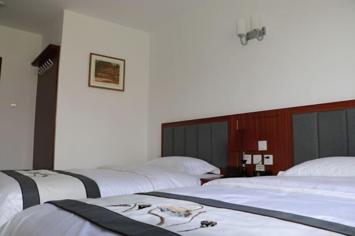 Habitación de hotel con dos camas, cabecero de madera, lámpara de pared e imagen enmarcada.