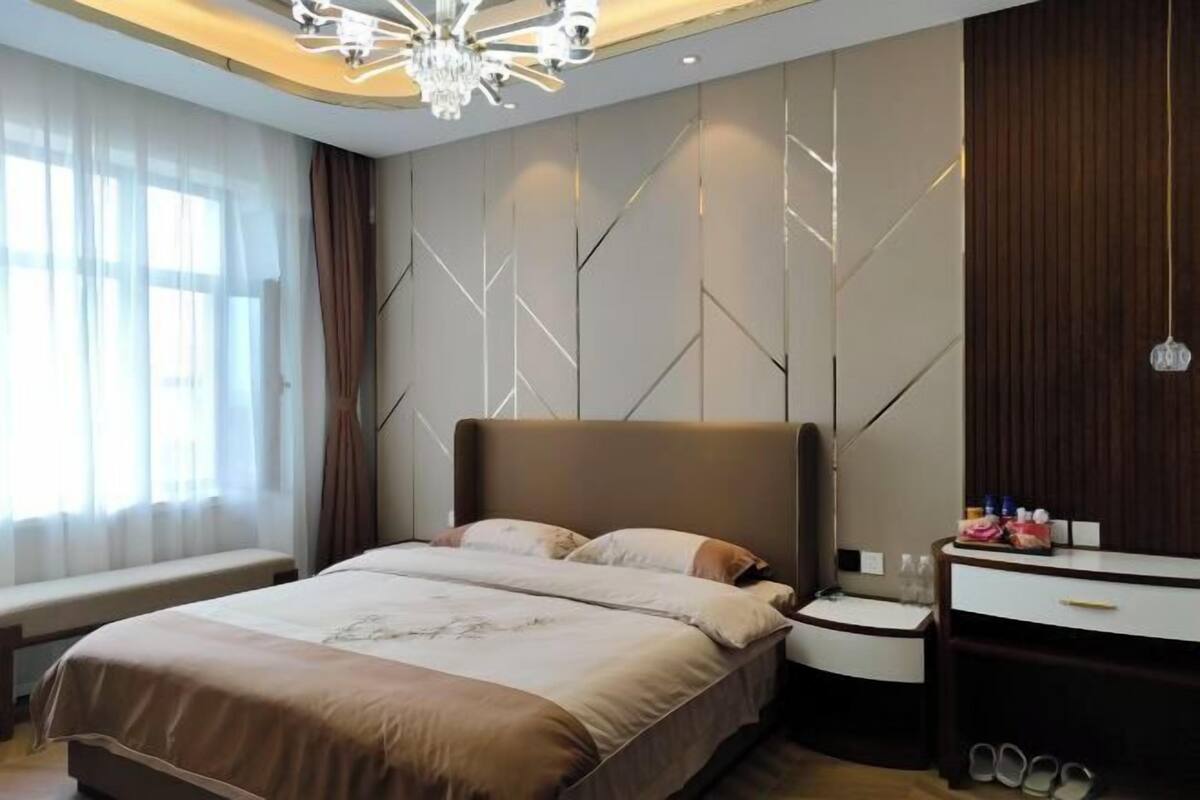 A modern bedroom with a large bed, a bedside table, a dresser, and a chandelier.