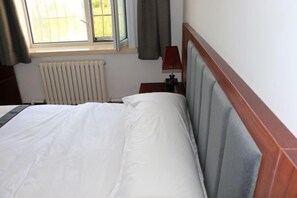 Una habitación de hotel con una cama, una ventana con cortinas, una mesita de noche con lámpara y un radiador.