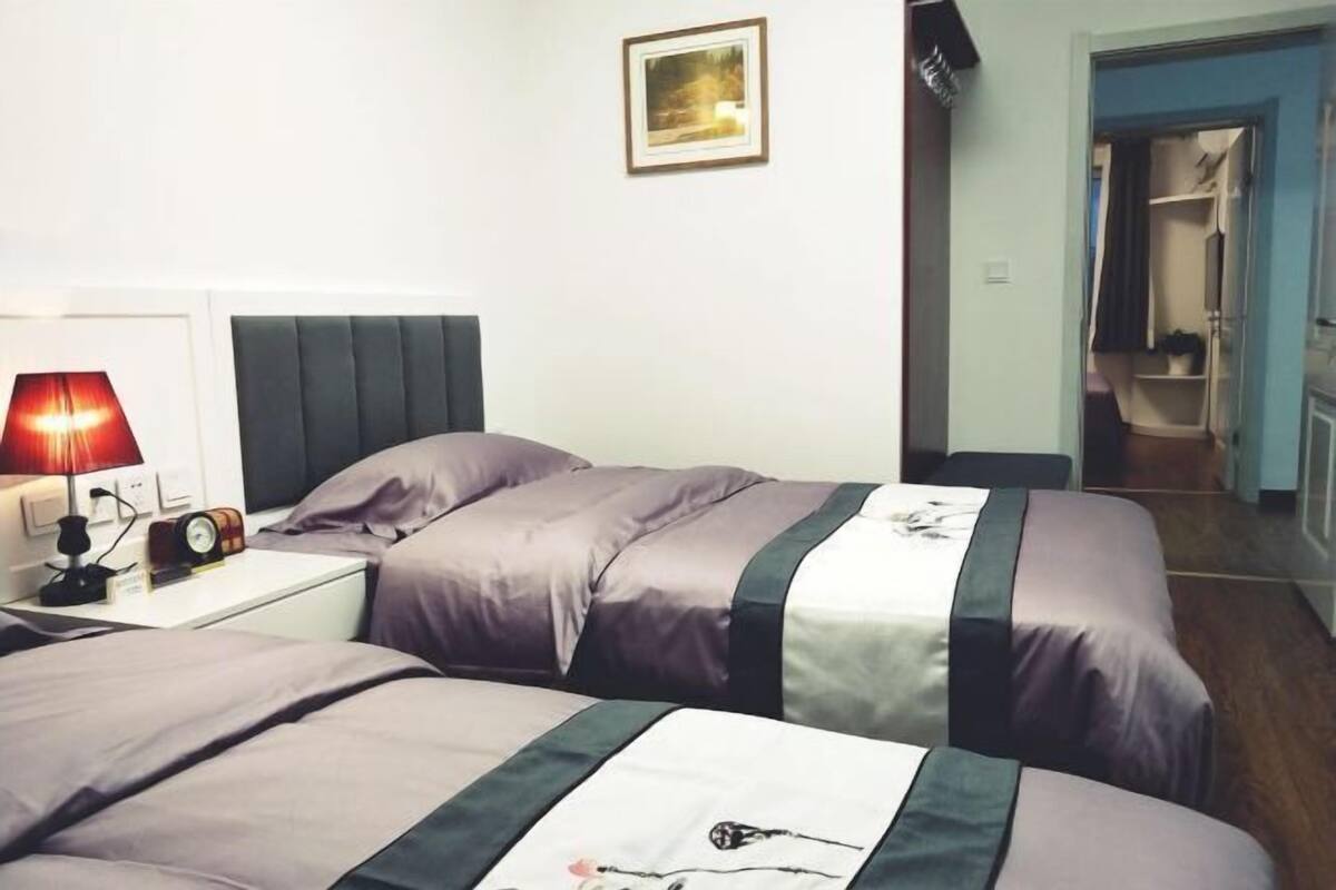 A room with two beds, a nightstand with a lamp, a framed picture on the wall, and a door leading to a bathroom.