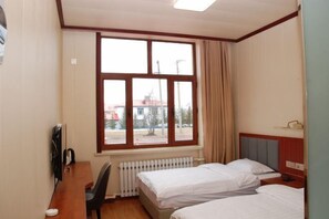 Habitación de hotel con dos camas, un escritorio, una silla, un radiador y una ventana con cortinas.