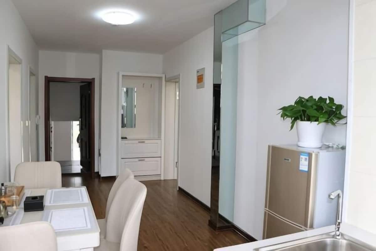 A hotel room with a kitchenette, a dining area, a mirror, and a potted plant.