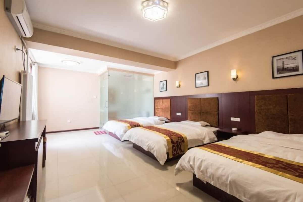 A hotel room with three beds, a desk, and a large window.