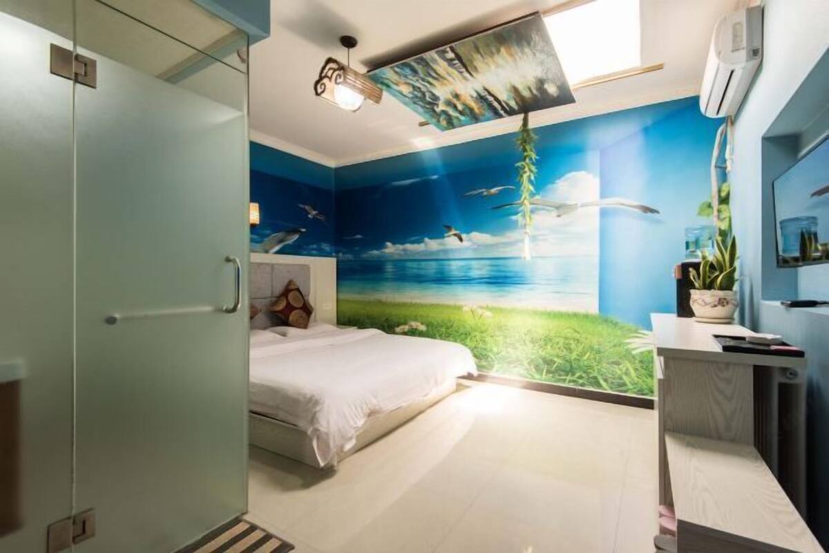 A bedroom with a bed, a desk, and a mural of a beach scene.