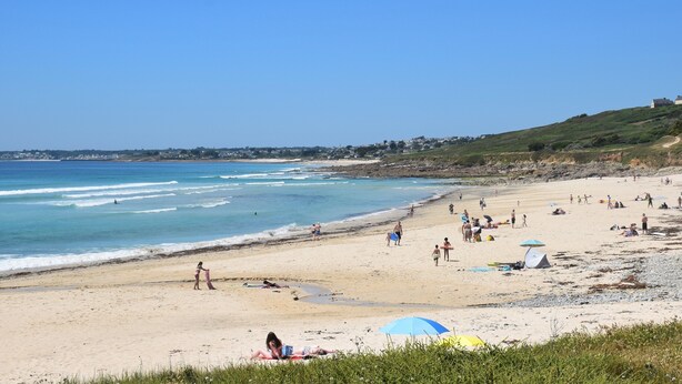 Una spiaggia con persone che prendono il sole, passeggiano e fanno surf.