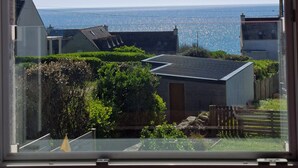 Vista dalla finestra su una zona residenziale, cielo sereno, costa in lontananza e un mix di architettura moderna e tradizionale.