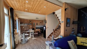 Un'ampia zona giorno con soffitto in legno, una scala e un'accogliente angolo salotto.