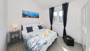 A bedroom with a bed, a nightstand, a ceiling fan, a window with curtains, and a painting on the wall.