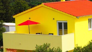 A yellow building with a red roof, a red umbrella, and a view of a body of water and hills in the background.