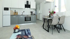 A modern kitchen with white cabinets, a built-in oven, and a dining area with a table and chairs.