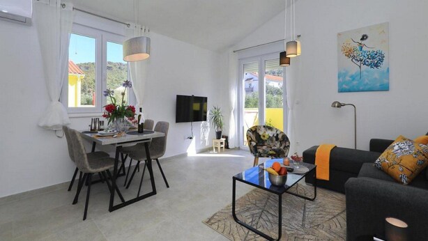 A modern living room with a dining area, a sofa, a coffee table, and a TV mounted on the wall.