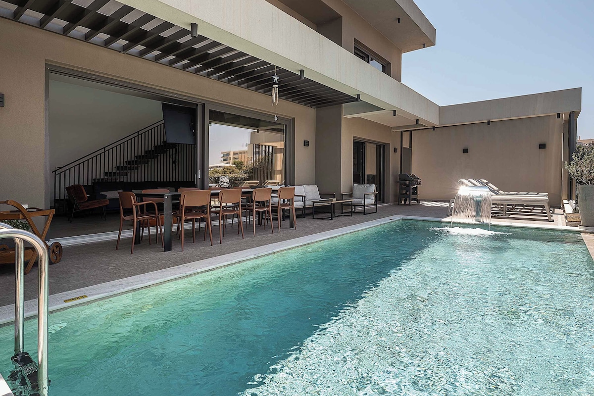 A swimming pool with lounge chairs and a barbecue area, surrounded by a building with a covered patio.
