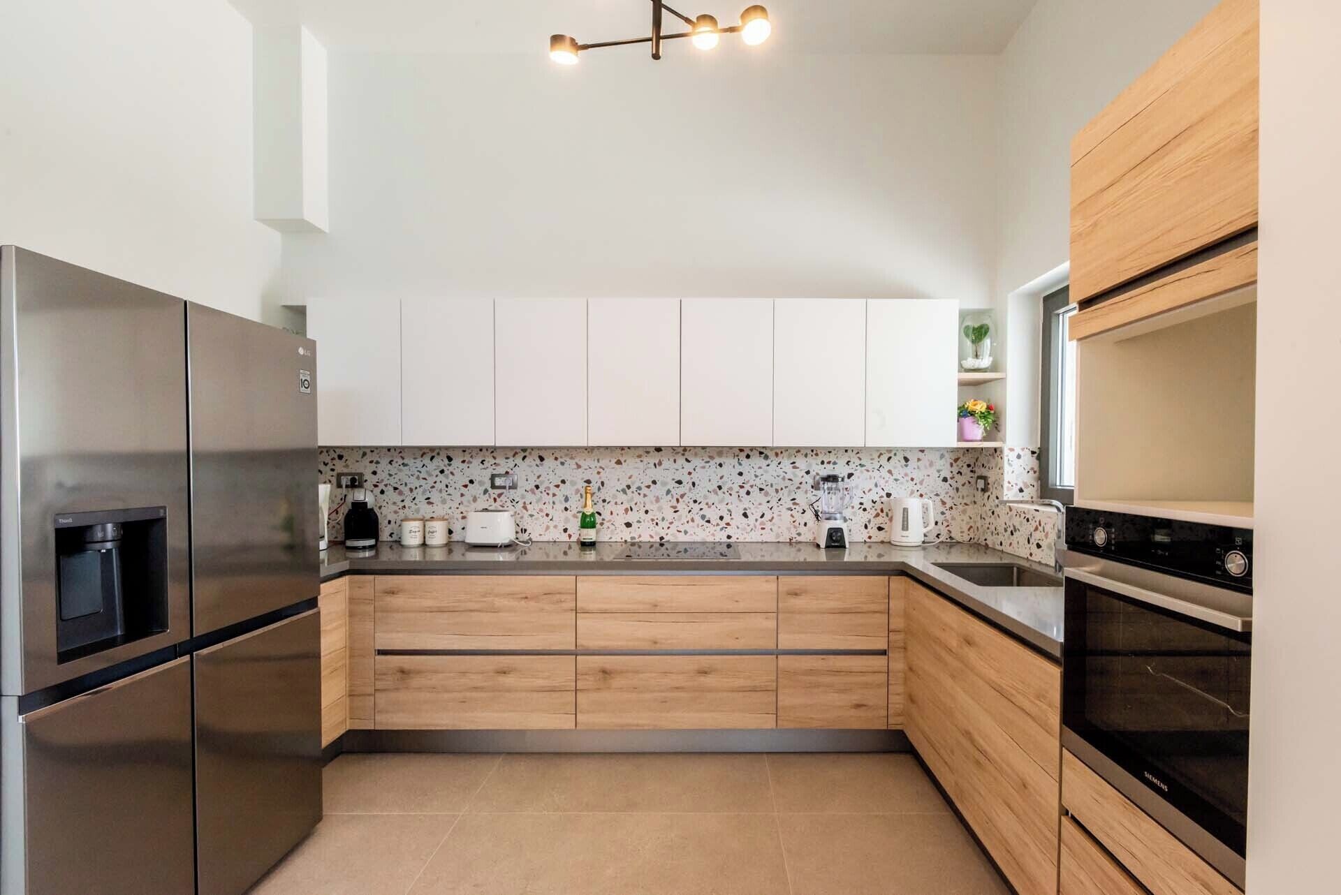 A modern kitchen with stainless steel appliances, wooden cabinets, and a speckled backsplash.