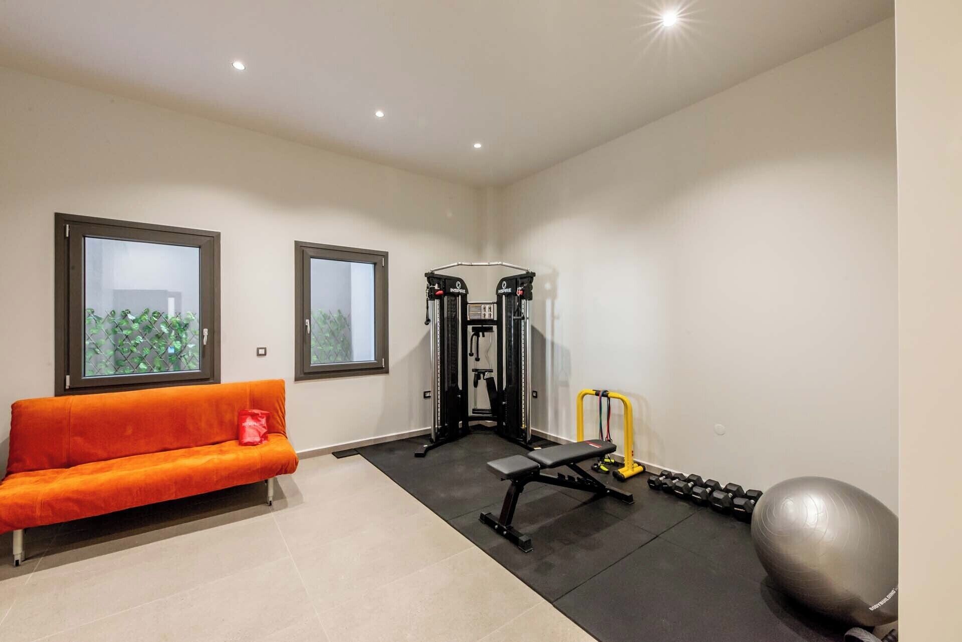A home gym with a bench, dumbbells, a medicine ball, and a squat rack.