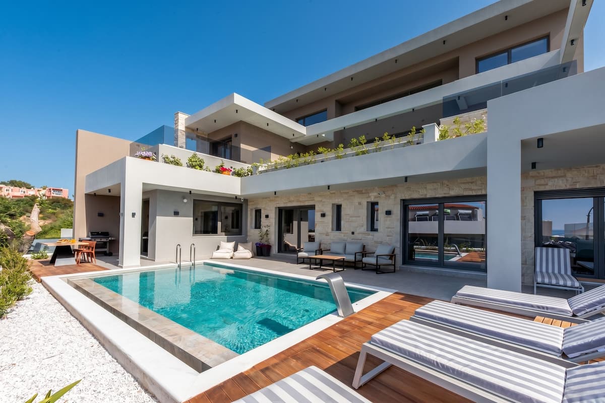 A modern multi-story building with a swimming pool, outdoor seating, and a view of the sea.