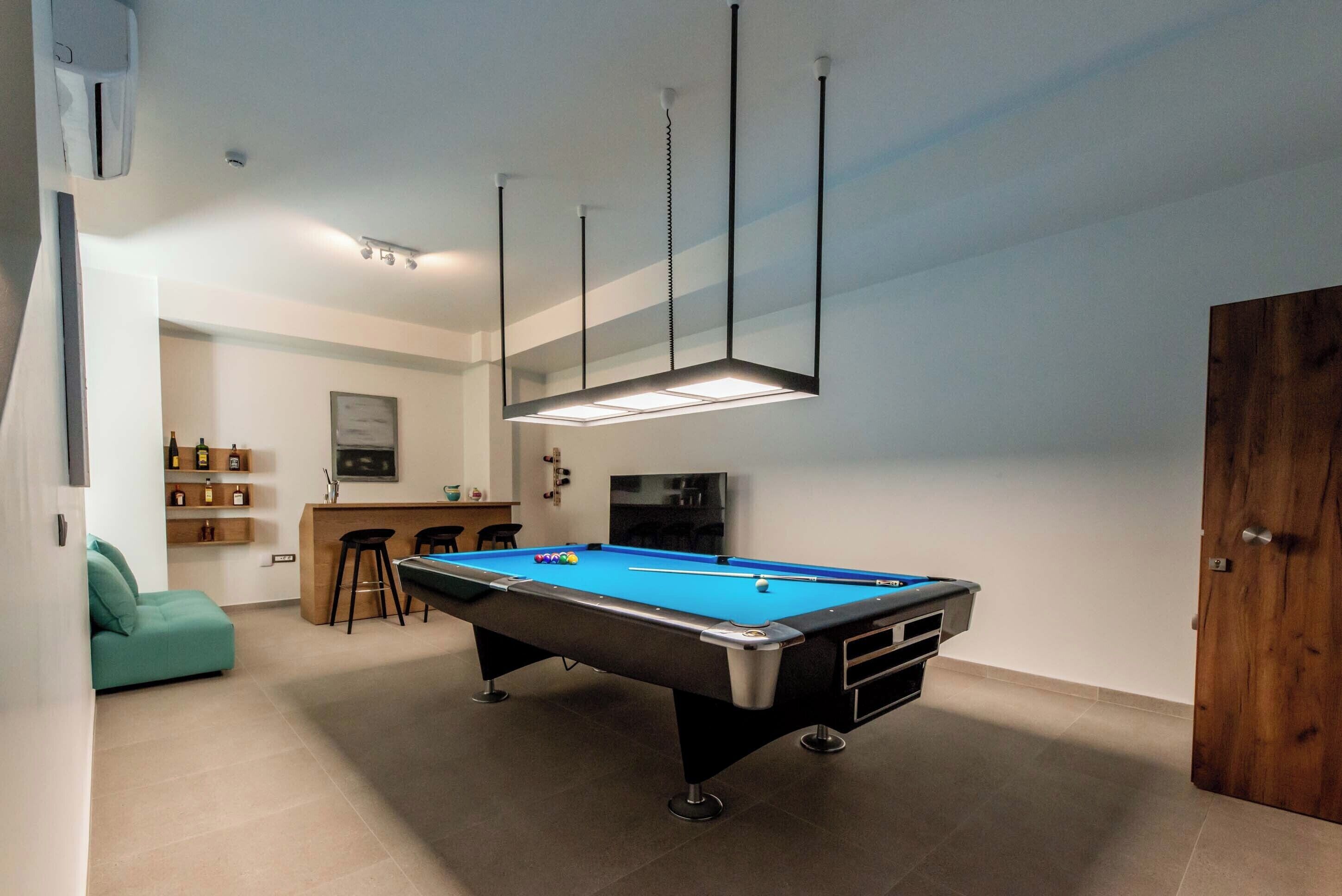 A pool table in a room with a bar area, a sofa, and a wooden door.