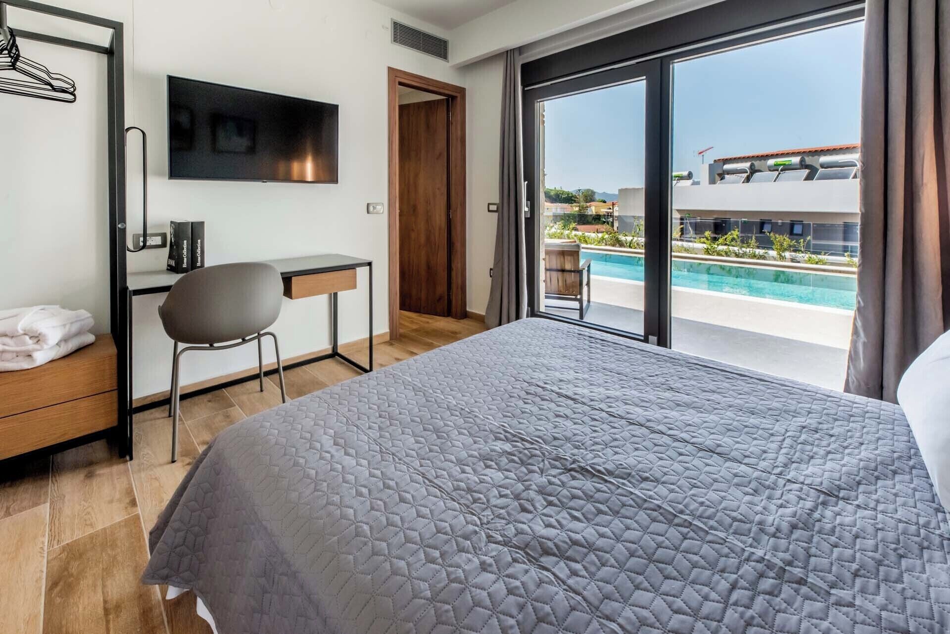 A hotel room with a bed, a desk, a chair, a TV, and a view of a swimming pool.