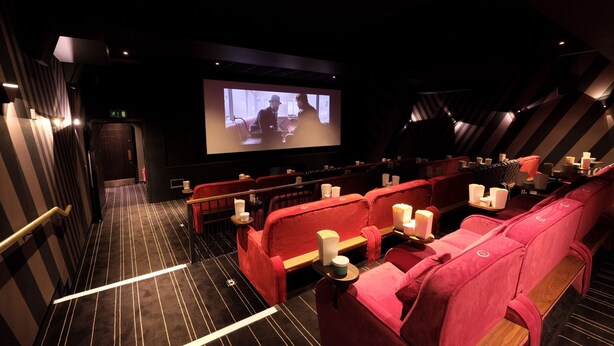 A cinema with red seats, a large screen, and a staircase leading to an exit.