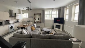 A modern living room with a grey sofa, a flat-screen TV, and a dining area with a table and chairs.