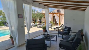 Une terrasse ensoleillée, dotée de mobilier noir, une piscine et une vue sur un immeuble avec balcon.