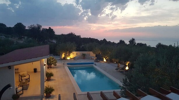 Une villa moderne dotée d’une piscine, d’un espace extérieur aménagé et offrant une vue sur la mer au crépuscule.