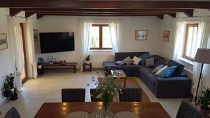 Un salon doté d’un grand téléviseur à écran plat, d’un canapé de couleur sombre agrémenté de coussins, d’une table basse en bois et d’une table à manger avec des chaises.