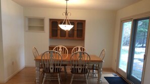 Comedor con mesa y sillas de madera, una lámpara de araña y vistas a través de un ventanal.