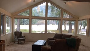Una habitación amplia con ventanas grandes, un sofá de cuero marrón, un sillón a juego y un pequeño reposapiés.