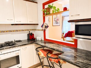 Una cocina con armarios blancos, estufa a gas, microondas y ventana con marco rojo.