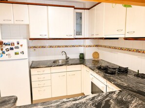 Cocina con armarios blancos, encimera de granito, pileta, estufa y refrigerador con imanes.