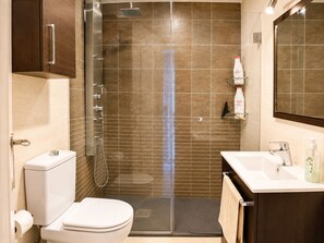 A modern bathroom with a glass shower enclosure, a toilet, a sink with a mirror, and toiletries.