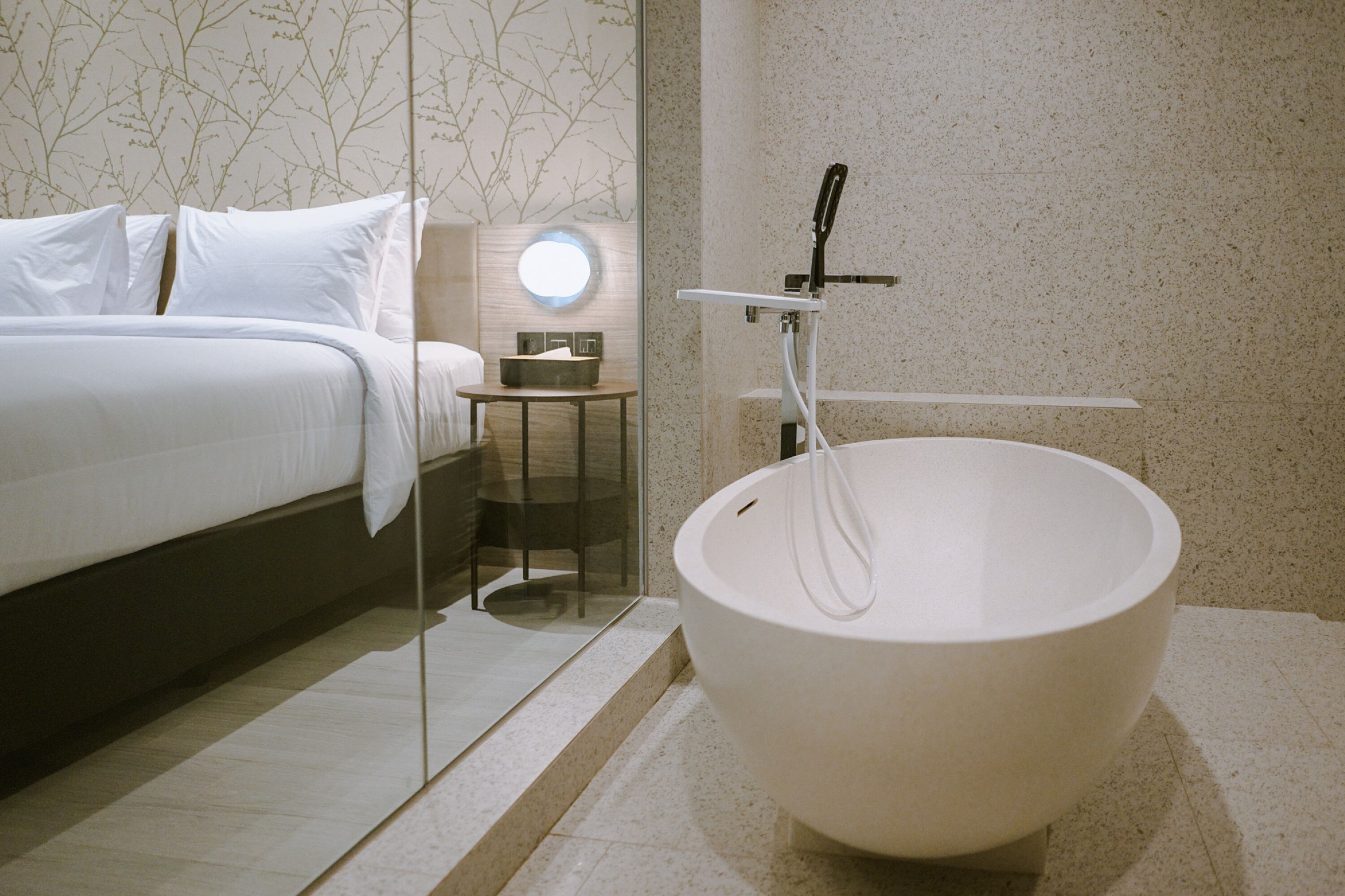 Une chambre à coucher moderne avec une grande baignoire ronde, un lit soigneusement fait et une petite table de chevet avec une lampe.