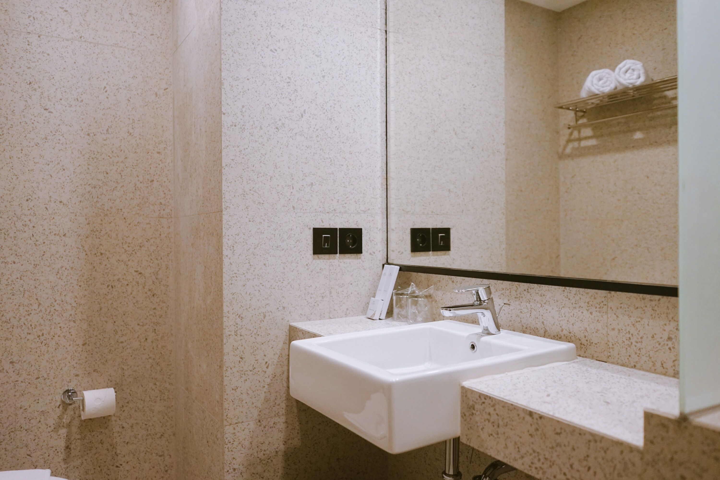 Un baño con un lavamanos blanco, un espejo y un perchero para toallas con toallas.