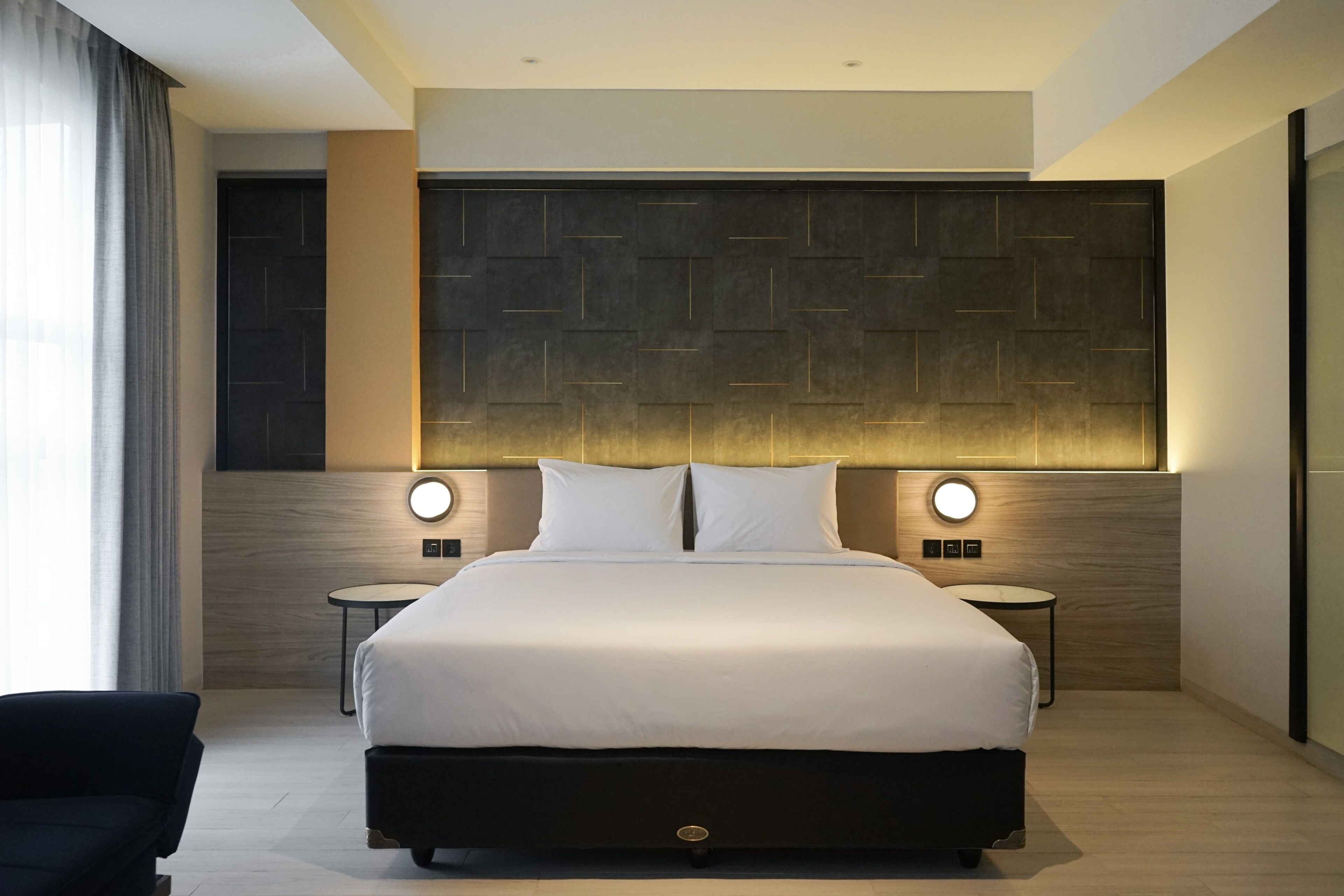 A modern hotel room with a large bed, two bedside tables, and a headboard with integrated lighting.