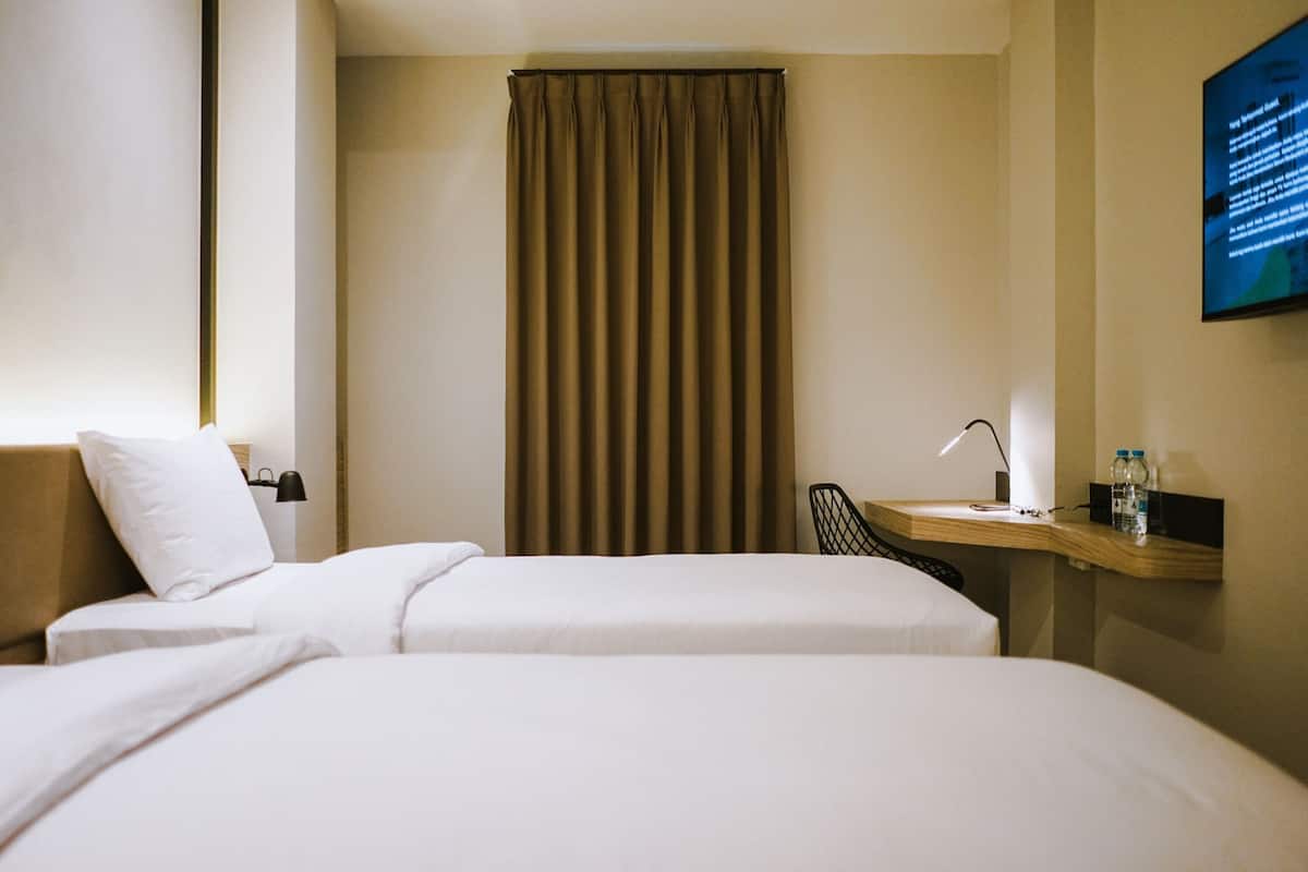 Habitación de hotel con dos camas, un escritorio con silla, una lámpara y un televisor en la pared.