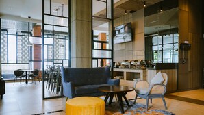 Un moderno espacio lounge con sofá, reposapiés y sillones, una estación de café y ventanas amplias con vistas.