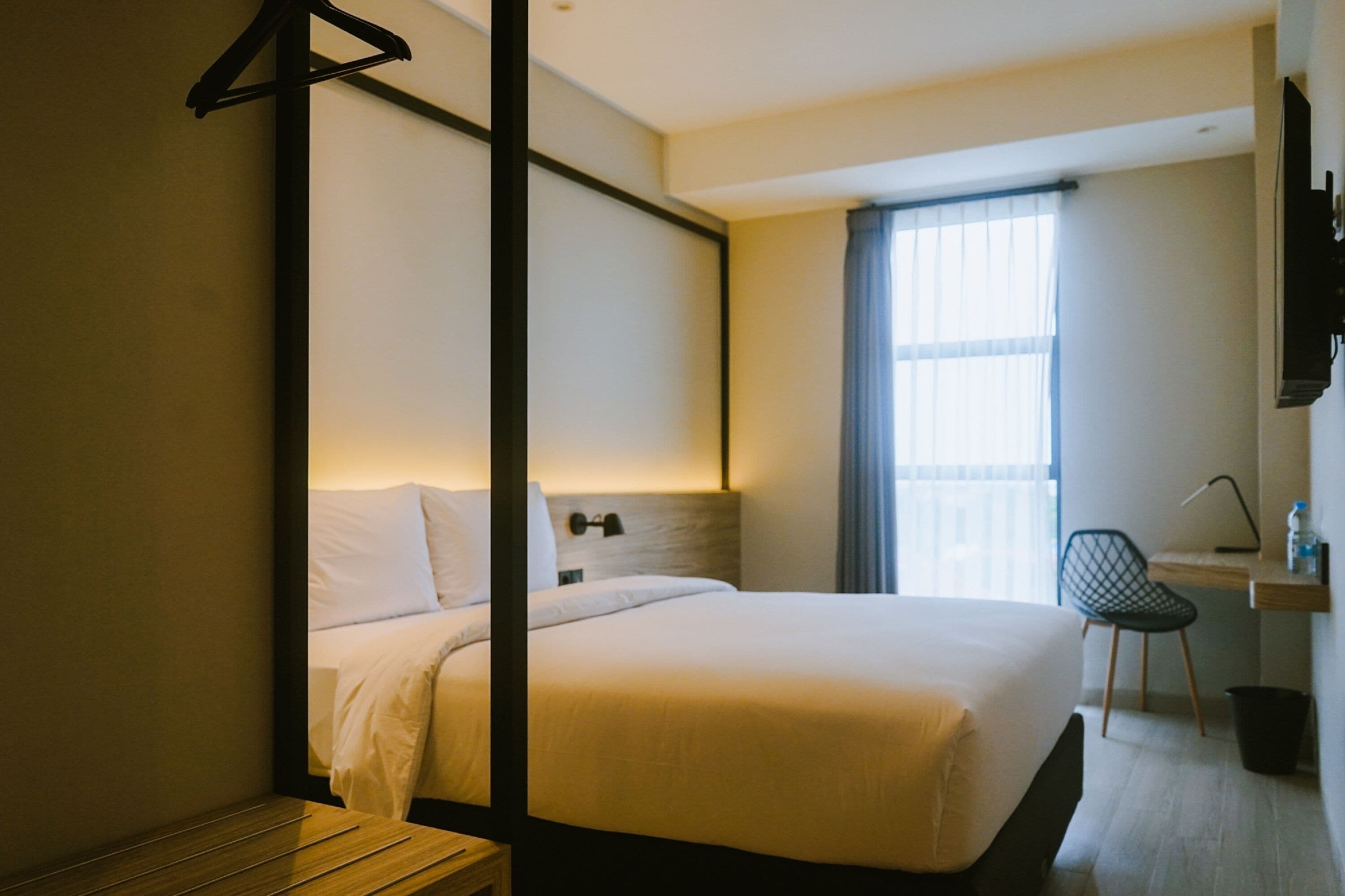 Habitación de hotel con cama, mesita de noche, silla, escritorio y ventana con cortinas.
