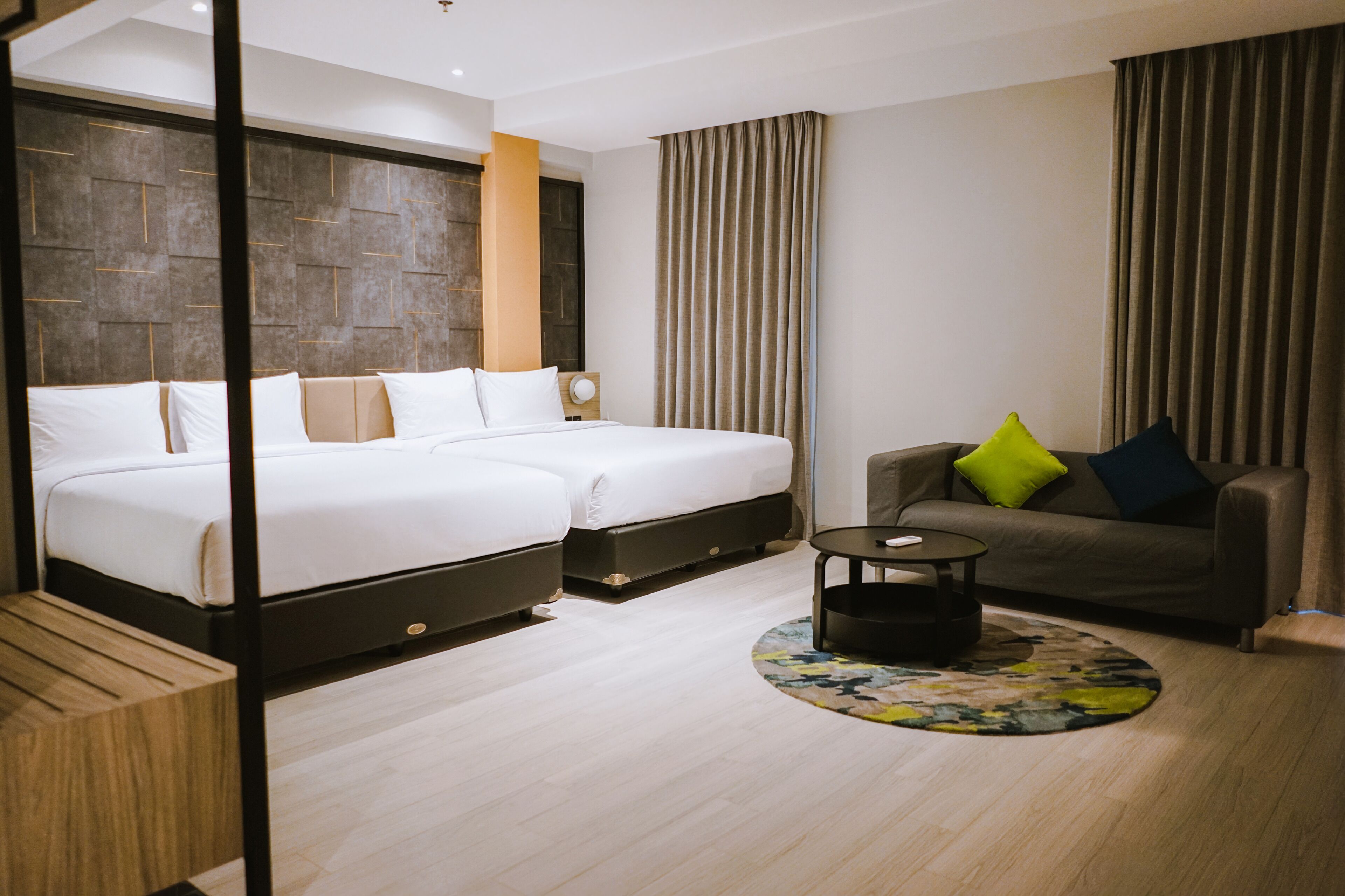 Een hotelkamer met twee bedden, een bank, een kleine ronde tafel en een kamerkleed met dessin.