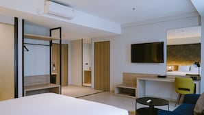 Una habitación de hotel moderna con cama, escritorio, silla, televisor y armario.