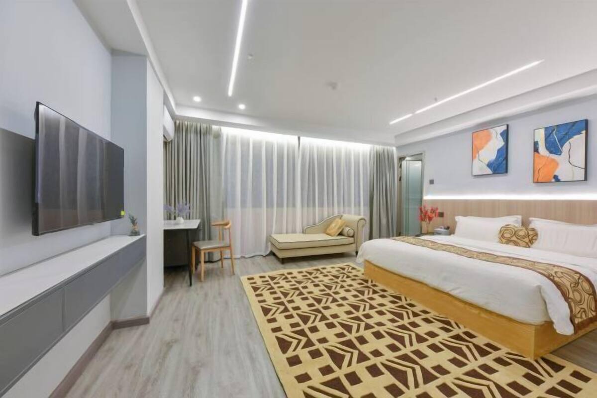 A modern hotel room with a large bed, a desk, a TV, and a view of the city.