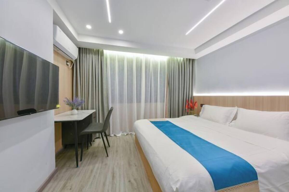 A hotel room with a bed, a desk, a chair, a TV, and curtains.