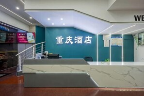 A hotel reception area with a teal wall, a reception desk, and a staircase leading to an upper level. - Chongqing Hotel (Shenzhen Luohu Port Guomao Subway Station) (Shenzhen)